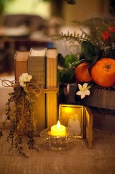 an arrangement of books, candles and flowers are on the table in front of some oranges