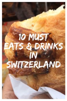 a person holding up a sandwich with the words 10 must eats & drinks in switzerland