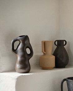 three vases sitting on top of a white shelf next to a black mug and a brown one