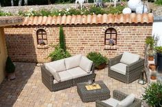 an outdoor patio with furniture and plants on the ground near a brick wall, surrounded by potted plants