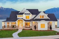 a large white house with lots of windows in front of the water and mountains behind it