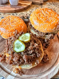 two hamburgers sitting on top of a wooden cutting board