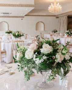 the centerpieces on this table are white roses and greenery