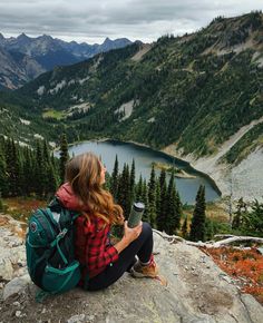 a woman sitting on top of a rock next to a lake