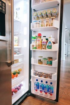 an open refrigerator door with food and drinks in the bottom shelf, inside it is a stainless steel fridge