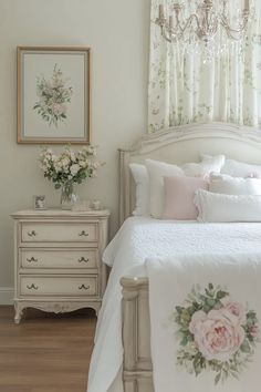 a white bed sitting under a window next to a dresser with flowers on top of it