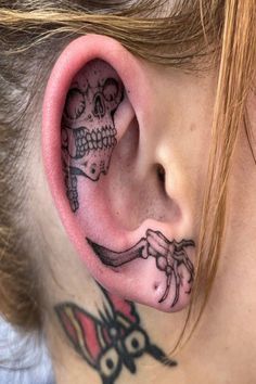 a woman with tattoos on her ear and behind the ear is a skeleton holding a knife