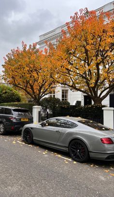 two cars are parked on the side of the road in front of trees with orange leaves