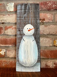 a painting of a snowman on a wood panel with brick wall in the background