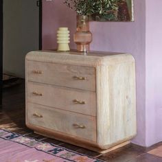 a wooden dresser sitting next to a purple wall with a vase filled with flowers on top of it