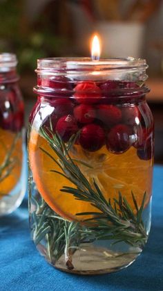 two jars filled with liquid and fruit on top of a blue table cloth next to a lit candle