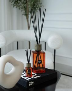 an orange bottle with reeds sitting on top of a table next to a white vase