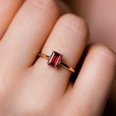 a woman's hand holding a ring with a red stone in the middle and gold band