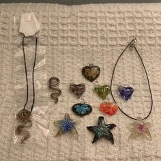 several different necklaces are laying on a bed with white sheets and one has a heart shaped glass pendant