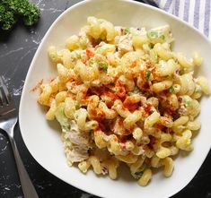 a white bowl filled with macaroni salad on top of a black table next to silverware