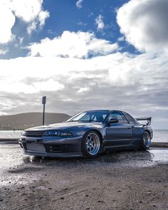 the car is parked on the side of the road next to the water and clouds