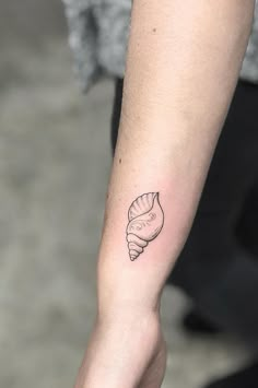 a woman's arm with a small tattoo of a seashell on the wrist