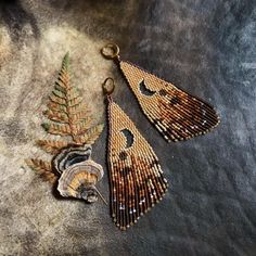 two brown and black beaded earrings sitting on top of a stone floor next to a leaf