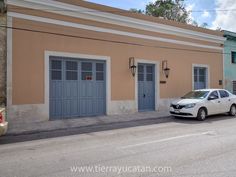 a white car parked in front of a tan building with two blue doors and windows