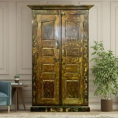 an old wooden armoire in a room with a blue chair and potted plant