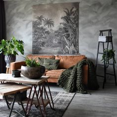 a living room with a couch, table and potted plants in front of a painting on the wall