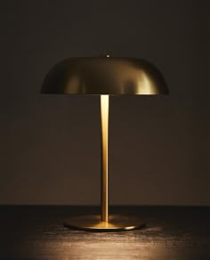 a table lamp sitting on top of a wooden table next to a black wall and floor