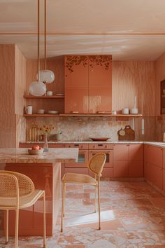 a kitchen with pink cabinets and marble counter tops, two chairs in front of the island