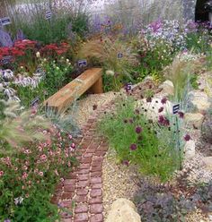 a garden filled with lots of flowers and plants next to a wooden bench in the middle