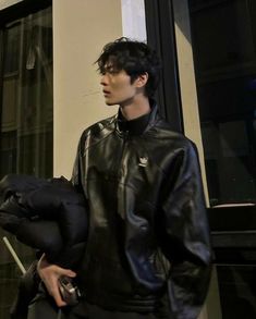 a man in a black leather jacket is holding a bag and looking off into the distance