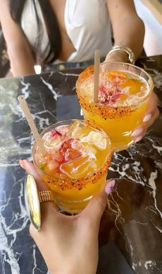 two people holding up glasses with drinks in them on top of a marble countertop