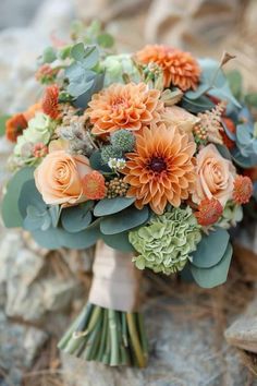 a bridal bouquet with orange flowers and succulents sits on some rocks