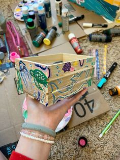 a person holding up a box that is covered in crafting supplies