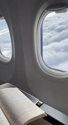 an open book sitting on top of a table in front of two windows above the clouds