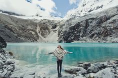 a woman standing on rocks in front of a mountain lake