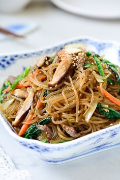 a bowl filled with noodles and veggies on top of a white table cloth