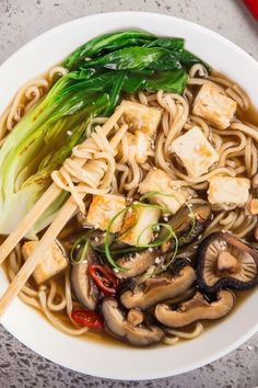 a white bowl filled with noodles and vegetables next to chopsticks on a table