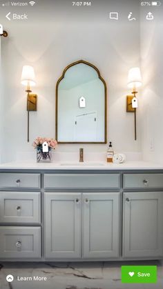 a bathroom with gray cabinets and marble counter tops, along with a gold framed mirror