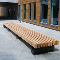 a wooden bench sitting on top of a brick walkway next to a building with large windows