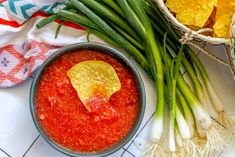 a bowl of salsa with tortilla chips on the side and green onions next to it