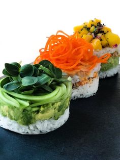 three different types of sushi on a black plate with green and orange toppings