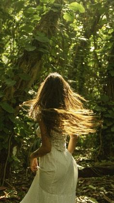 a woman in a white dress is walking through the woods with her hair blowing in the wind