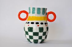 a white and green checkered vase with an orange ring on the handle is shown