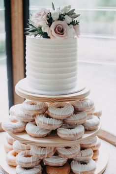 a three tiered white cake with frosting and flowers on top is surrounded by donuts