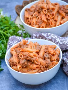 two white bowls filled with penne alla and ground beef on top of a blue table