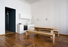 an empty room with a wooden table and bench in the center, next to a stove