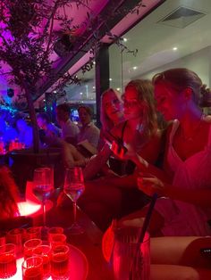 several women sitting at a table with wine glasses and candles in front of them, all looking at their cell phones