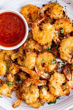 a white plate topped with fried shrimp next to a bowl of ketchup and dipping sauce