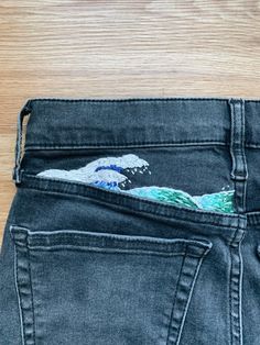 the back pocket of a pair of jeans with an image of a wave painted on it