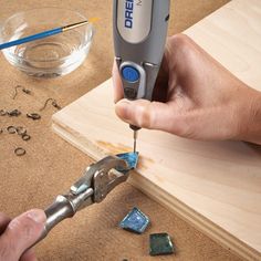 a person is using a drill to cut glass pieces on a table with other tools