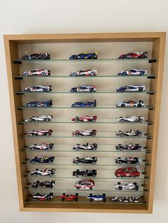 a display case filled with lots of different types of toy cars on glass shelves in front of a white wall